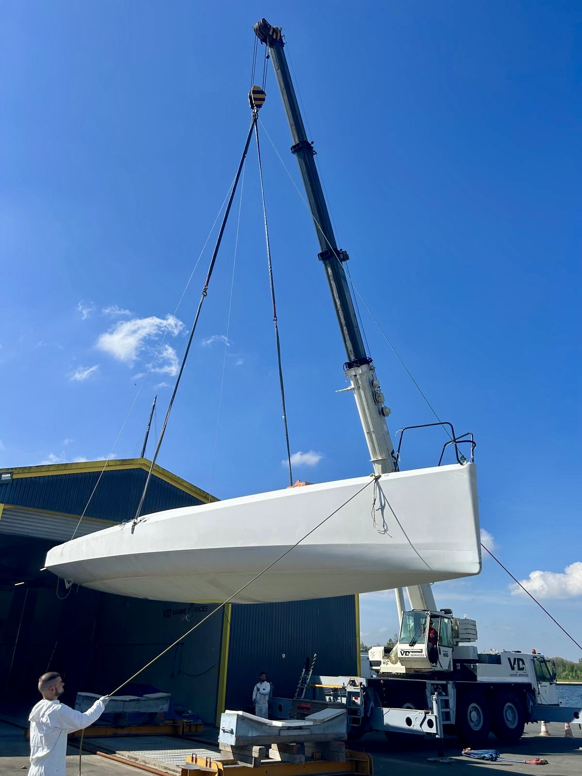 Guerrera suspended by crane against a blue sky, crew handling lines below
